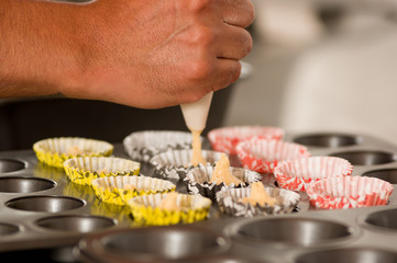 A bakery man is preparing a delicious christmas cookies in a bakery store, adding Dough inside of the cupcake Wrappers