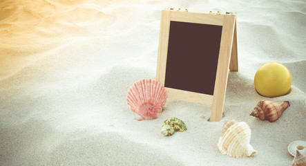 Happy smiley face ball, seashell and blank blackboard for text on clean sand beach. Beach accessories on sand beach.