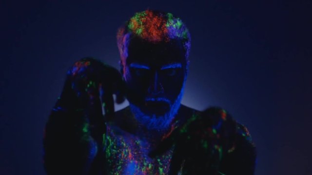 A man with a beard in the ultraviolet light. Magic passes with hands.