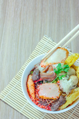 Pink seafood flat noodles (Tom Yum Yen-Ta-Fo) with fish ball and dumpling fish, special homemade red sauce serve in white bowl on wooden table, Top view