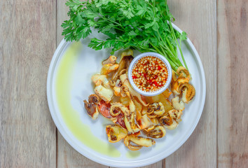 Grilled squid and vegetable with seafood sauce in white plate on wooden table