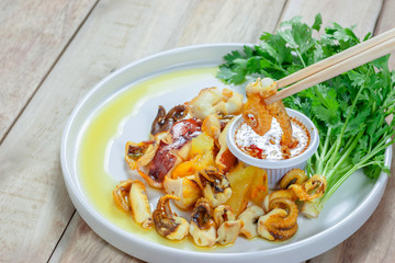 Grilled squid and vegetable with seafood sauce in white plate on wooden table