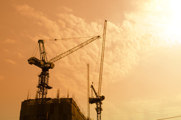 Industrial construction cranes and building silhouettes over sun at sunrise.