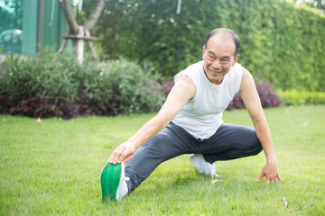 Asian old man stretching leg on mat in field, outdoor exercise concept.