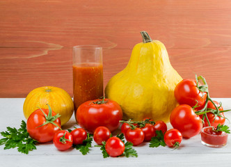 Still life of tomato and pumpkin with green leaves on a wooden background