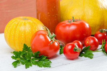 Composition of large tomatoes, cherry, pumpkin, and a glass of juice on a paternal background.