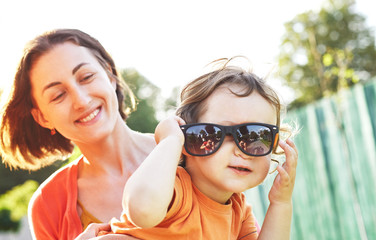 Family with child walks and plays in city park. A young father, mother and a small son dressed in orange t-shirt. The child funny dresses up sunglasses and plays with them. Child in the hands of his