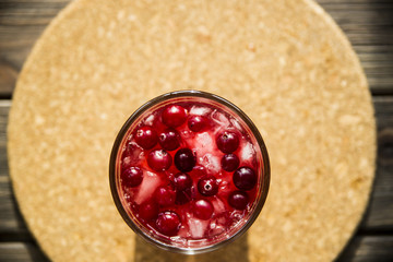Cranberry mors with ice and berries. On a wooden table and a round cork stand © svitlini