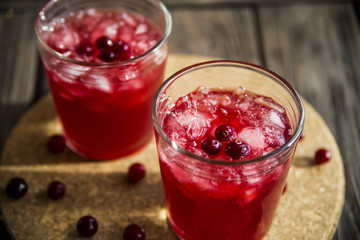 Cranberry mors with ice and berries. On a wooden table and a round cork stand © svitlini