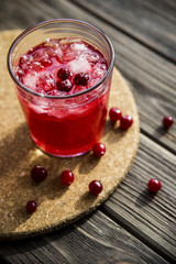 Cranberry mors with ice and berries. On a wooden table and a round cork stand © svitlini