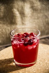 Cranberry mors with ice and berries. On a wooden table and a round cork stand © svitlini