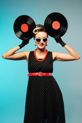 Pretty pin-up woman with retro hairstyle and make-up posing with vinyl record over blue background.