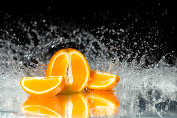 Fototapeta na wymiar Fresh orange on black background with streaming water on it. Mirrored ground. Water drops on fresh fruits. Freeze motion of water falling on fresh fruits.