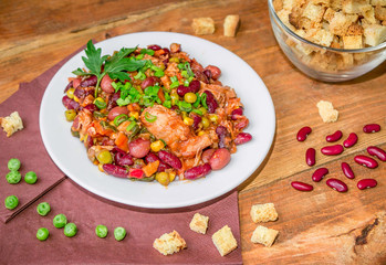Homemade Stewed beans with chicken meat green peas and vegetables served with cut green onion and parsley on a white plate and croutons on wooden table