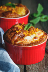 Close-up of two baked desserts with orange and mint in red cream-bowls on an old rustic wooden table