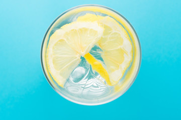 glass of blocked ice and lemon slice on blue background, top view