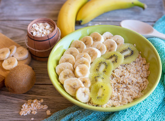 
Oatmeal with bananas for breakfast. Dietary food in a green plate with a spoon on a wooden background