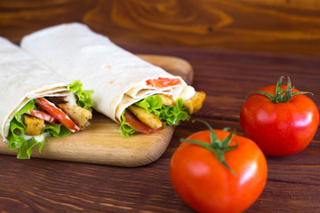 Fototapeta na wymiar Kebab with chicken. Shaurma with meat, cabbage, tomato, lettuce leaf, sauce on a wooden background. 