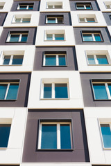 Fototapeta premium From below shot of modern and new apartment building. Photo of a tall block of flats against a blue sky.