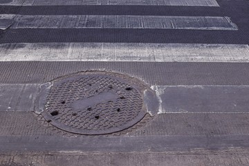 The zebra crossing and sewer cover in sunny day in Thailand
