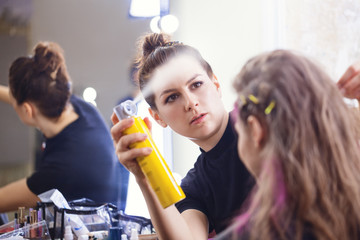Make-up artist applying hairspray on model's hair,  focus on make-up artist