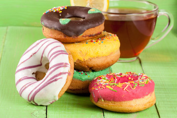 pile of glazed donuts with a cup of tea on a green wooden background