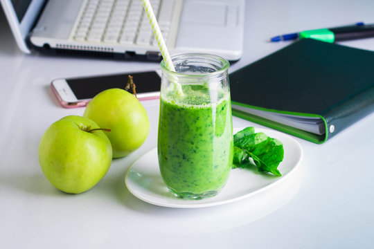 Workplace working table with laptop, computer, notebook, phone mobile smart phone, pen, marker. Healthy Drink Smoothie from Green Spinach and Apples