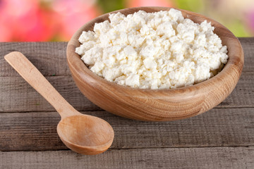 Cottage cheese in a wooden bowl on board with blurred garden background