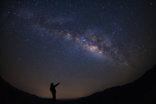 A Man is standing next to the milky way galaxy pointing on a bright star, Long exposure photograph, with grain.
