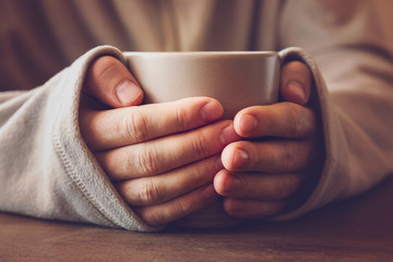 Man's hands holding a mug and warming with hot tea in the evening.