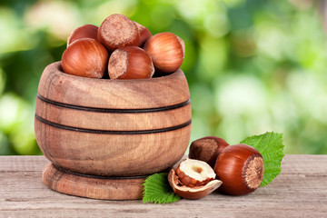 Hazelnuts with leaves in a wooden bowl on a wooden table with blurred garden background