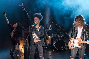 Female singer with microphone and rock and roll band performing hard rock music on stage