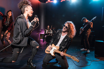 Female singer with microphone and rock and roll band performing hard rock music on stage