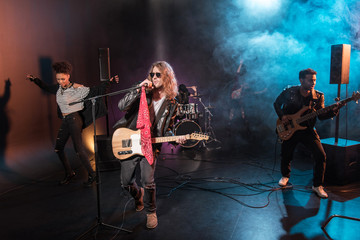 Male singer with microphone and rock and roll band performing hard rock music on stage