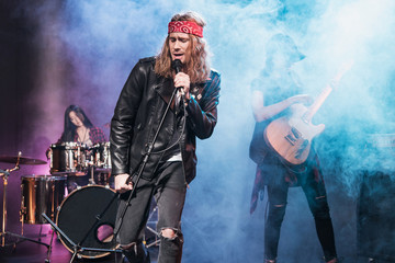 Handsome singer with rock and roll band performing music on stage