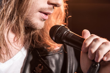 Cropped shot of young male singer with microphone on stage