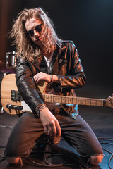 Fototapeta premium Handsome rock star in eyeglasses posing with electric guitar on stage