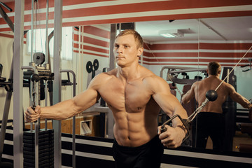 Fototapeta na wymiar Young strong athlete with a beautiful naked torso doing muscle exercises in the gym