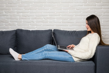 Happy woman sitting on couch using her laptop at home in the living room