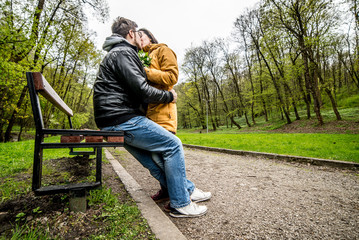 Fototapeta premium Man and woman embracing and kissing on bench in green spring park