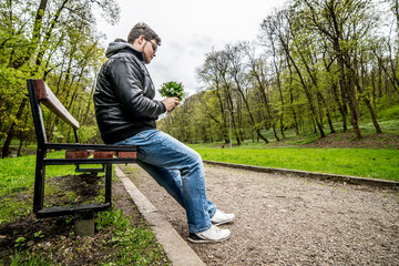 Young guy waiting for his date seated on bench in park