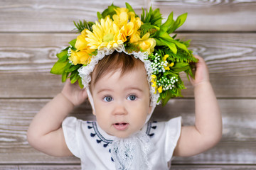 Portrait of a cute baby girl on a light background with a wreath of flowers on her head sitting on sofa basket