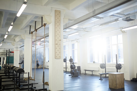 Background image of various equipment in gym: exercise stands with climbing rope and barbell benches in empty sunlit hall