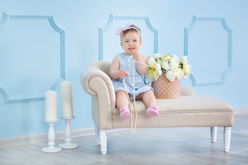 Portrait of a cute baby girl on a light background with a wreath of flowers on her head sitting on sofa basket