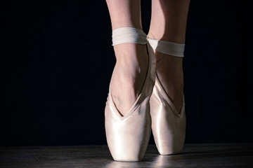 Close-up classic ballerina's legs in pointes on the black background and wooden grey floor.