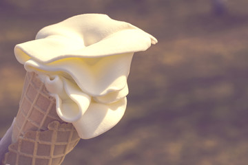 Waffle cone with creamy ice cream in the sun on a background of green grass