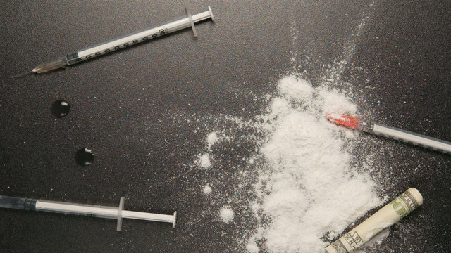 TOP VIEW: Heroin powder falls on a black table with syringes