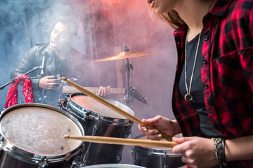 side view of woman playing drums and man singing into microphone, rock and roll band concept
