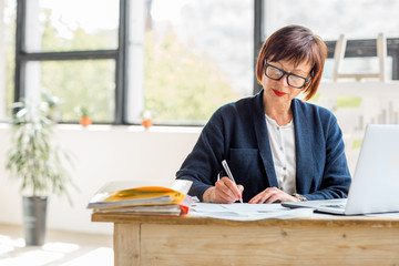 Senior businesswoman working with documents and laptop at the bright modern office interior