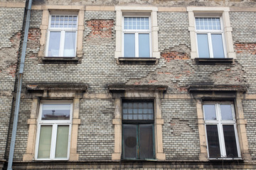 Six white Windows on the facade of the old damaged brick building with a drain pipe